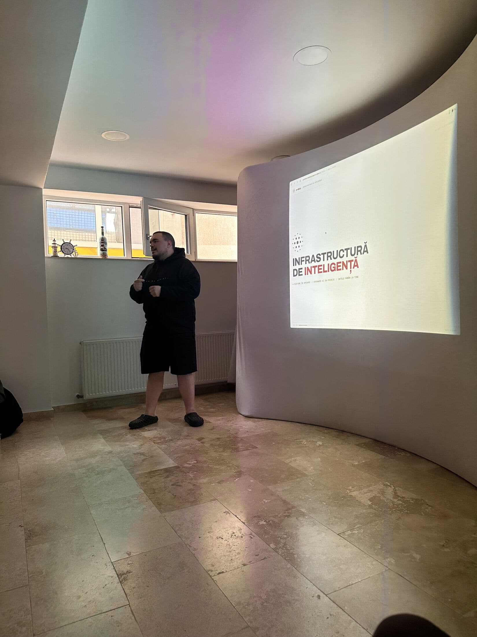 Prezentator e-data deschizând sesiunea, cu slide-ul „Infrastructură de inteligență” proiectat pe ecran