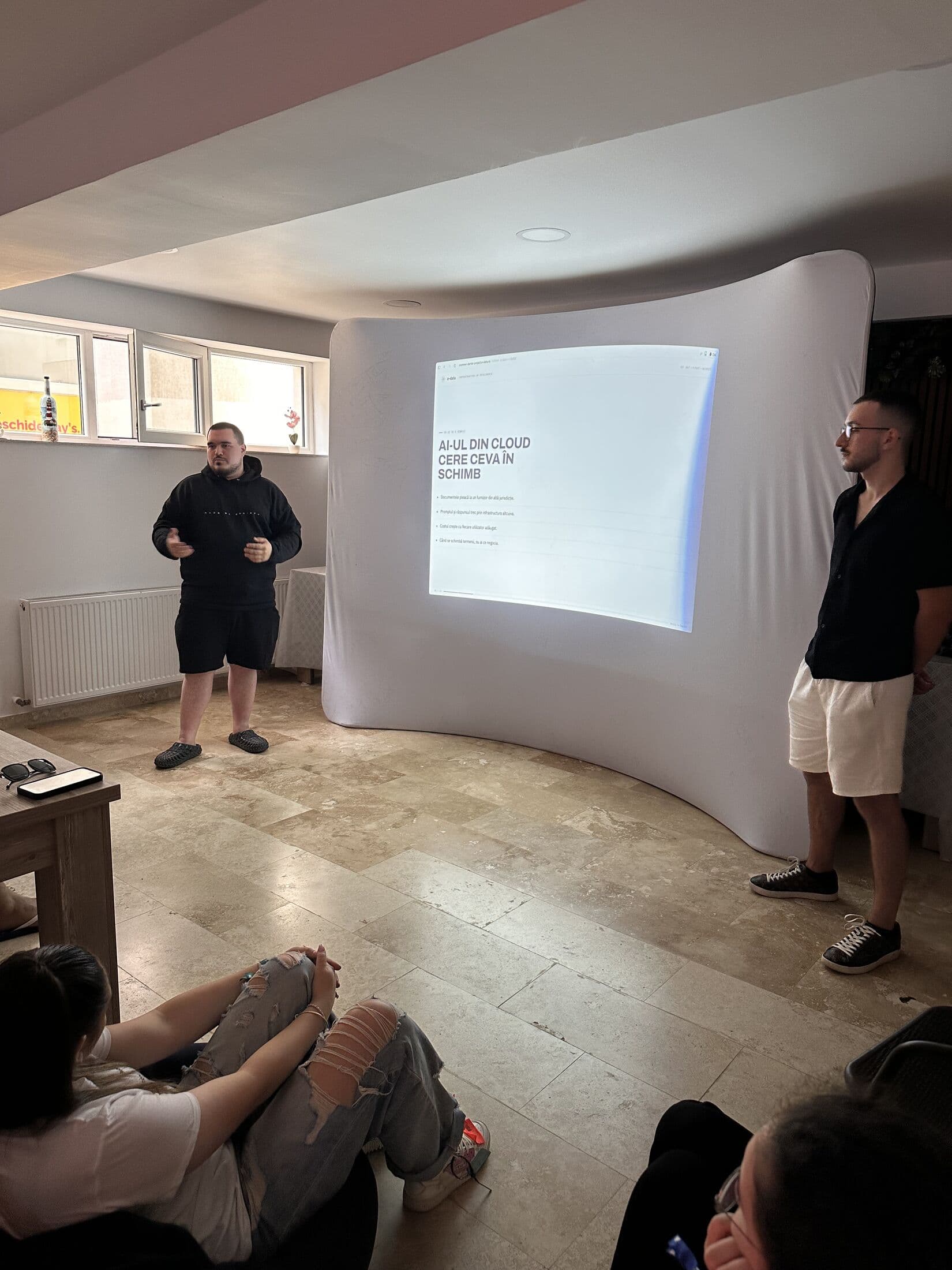 Doi prezentatori e-data în fața slide-ului „AI-ul din cloud cere ceva în schimb”