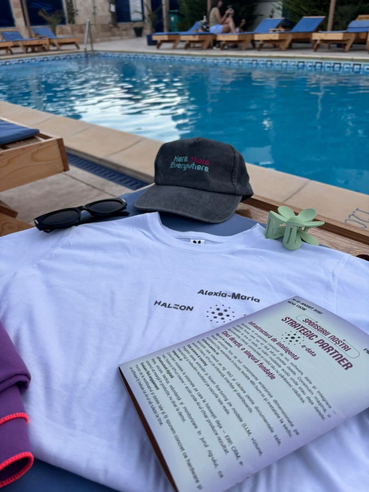 Tricoul evenimentului și broșura sponsorilor așezate pe un șezlong, lângă piscină